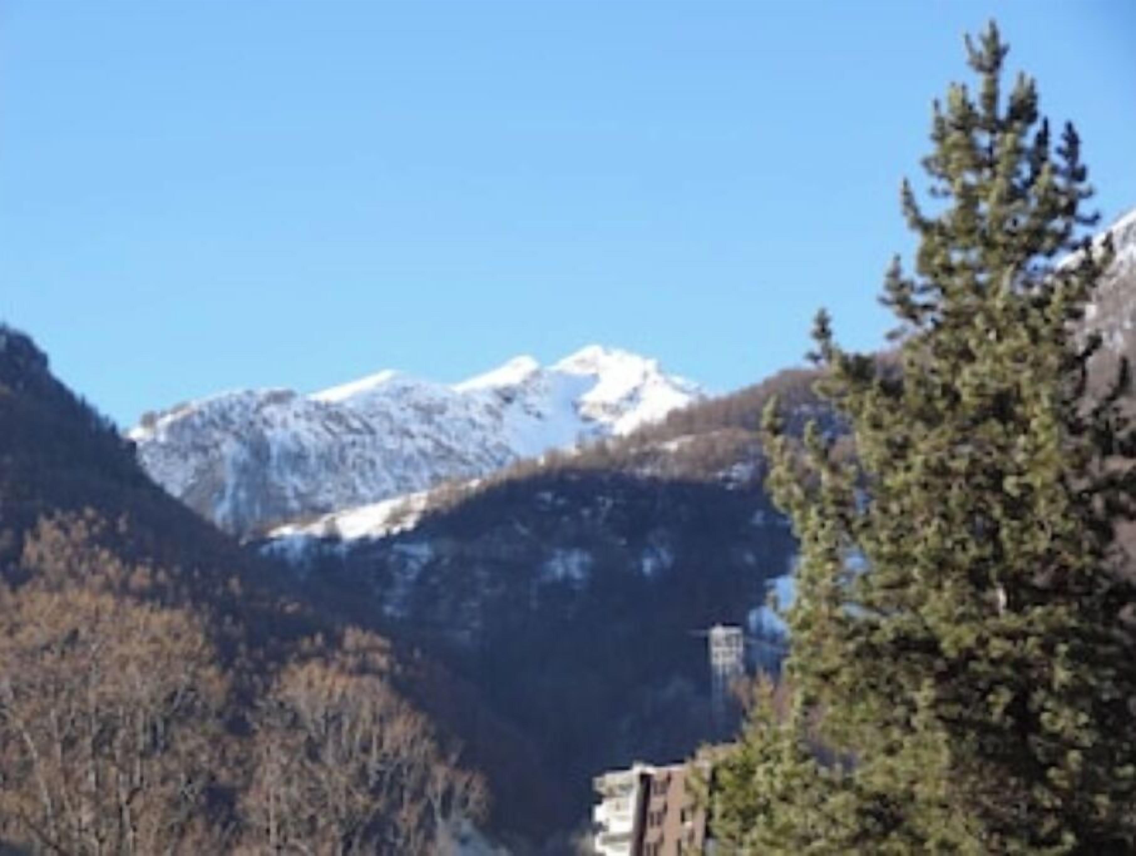 A mountain landscape with snow-capped peaks, a clear sky, and a building with a visible antenna.