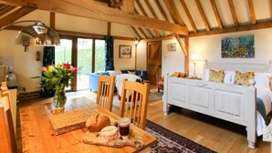 A cozy room with a wooden ceiling, a bed with colorful pillows, a dining table with bread and jam, and a painting on the wall. - Orchard Barn Spa, exclusively for you, New Forest (Sandleheath)