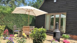 A wooden cabin with a patio area featuring outdoor furniture, a large umbrella, and potted plants. - Orchard Barn Spa, exclusively for you, New Forest (Sandleheath)