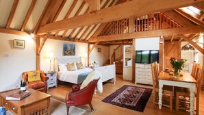 A spacious loft-style bedroom with a large bed, a red armchair, a wooden dining table, and a TV. - Orchard Barn Spa, exclusively for you, New Forest (Sandleheath)