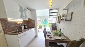 Una cocina moderna con armarios blancos, una encimera de madera y un comedor con mesa para dos.