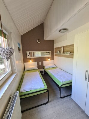 Een kamer met twee éénpersoonsbedden, een kleine tafel, een spiegel, een plank met decoratieve objecten en een radiator.