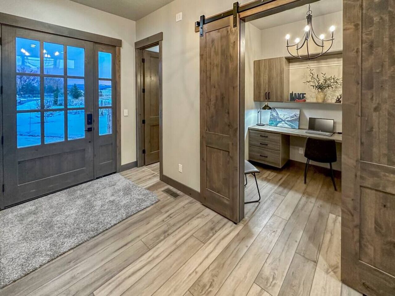 A modern kitchen with a large island, wooden flooring, and a sliding door leading to a dining area.