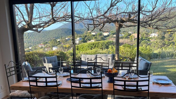 Un coin repas offrant une vue sur un village perché sur une colline, aménagé avec des chaises en métal et une table en bois, dressée pour quatre personnes.