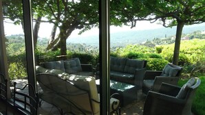 Une terrasse ensoleillée offrant une vue sur un paysage luxuriant, avec un espace salon comprenant une table et des chaises.
