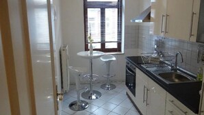 A compact kitchen with a window, a sink, a stove, and a small dining area with stools.