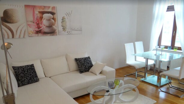 A modern living room with a white sofa, glass coffee table, and a dining area with a white table and chairs.