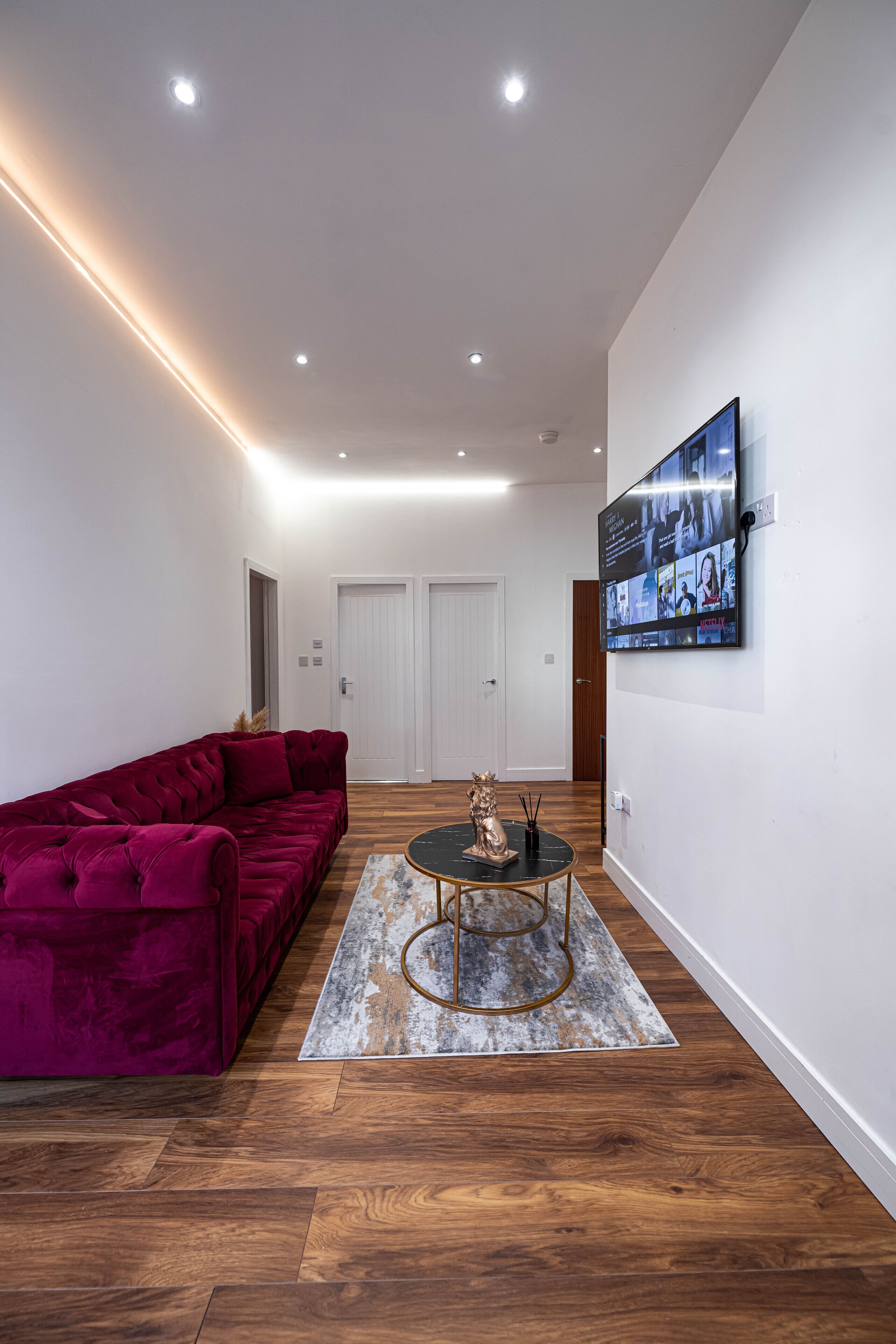 A modern living room with a red velvet sofa, a round coffee table, and a flat-screen TV mounted on the wall.