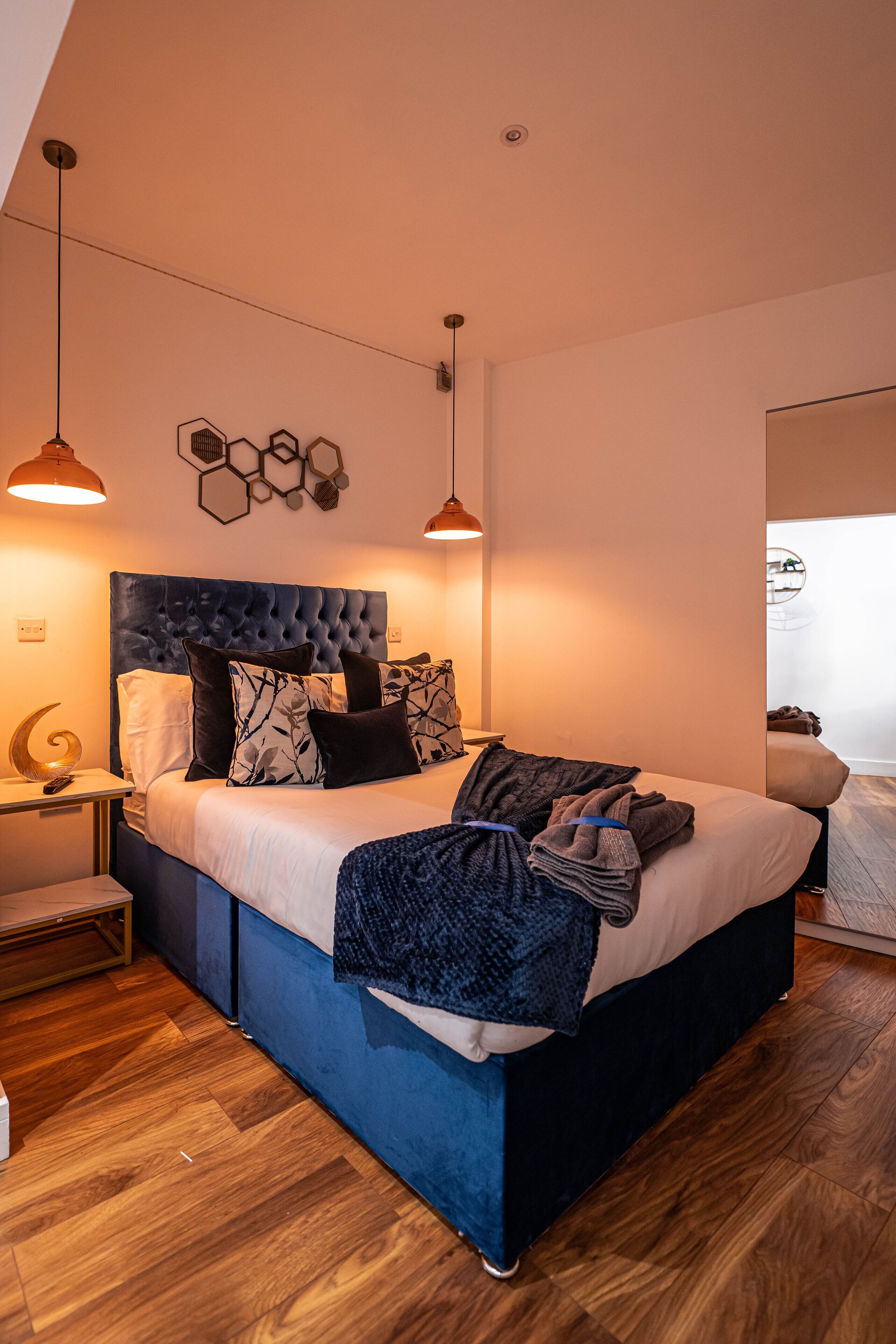 A modern bedroom with a tufted headboard, a wooden floor, and pendant lighting.