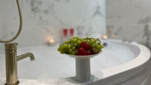 Un lavabo de salle de bain avec un pare-éclaboussures en marbre blanc, un robinet doré et un bol rempli de raisins verts et de fraises.