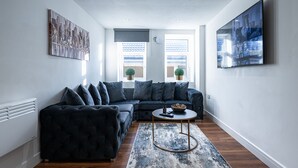 Un salon moderne avec un canapé d’angle aux couleurs sombres, une table basse ronde et un grand tableau abstrait accroché au mur.