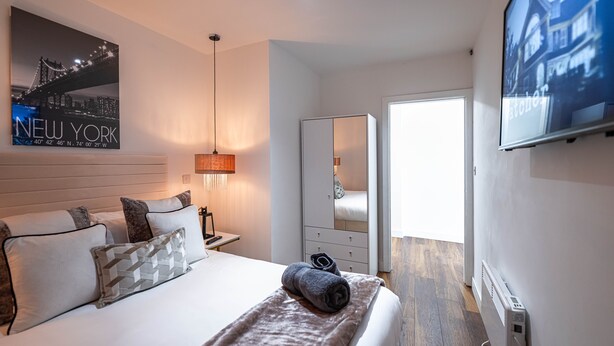 Une chambre d’hôtel avec un lit, un miroir, une télévision et une affiche représentant la ville de New York.