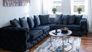 Un salon moderne avec un canapé d’angle aux couleurs sombres, une table basse ronde et un grand tableau abstrait accroché au mur.