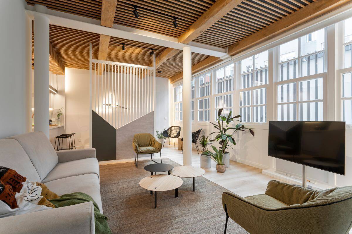 A modern living room with a sofa, two chairs, a TV, and a staircase.