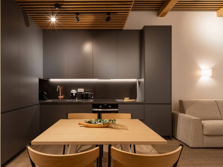 A modern kitchen with dark cabinetry, a wooden ceiling, and a dining area with a table and chairs.