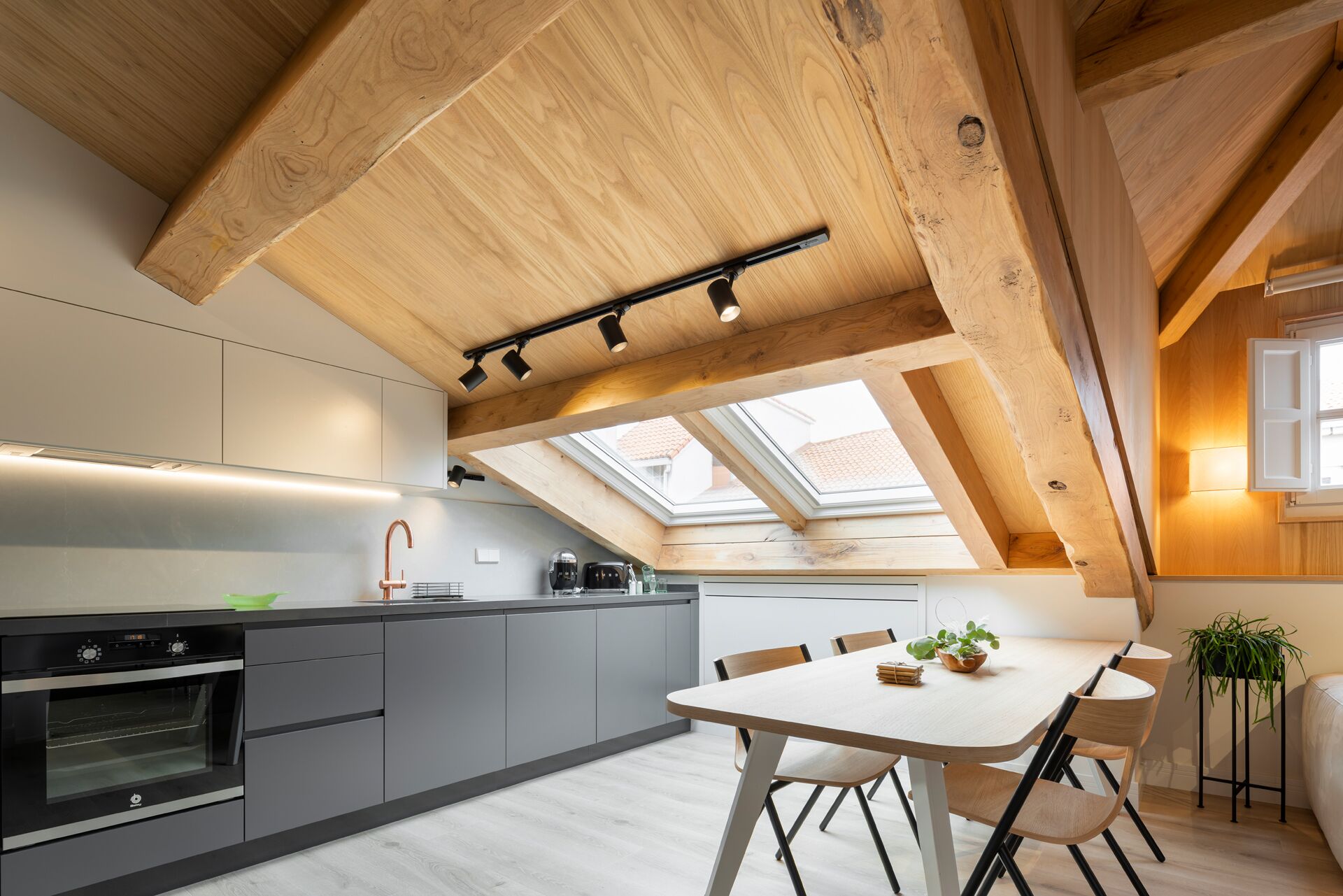 A modern kitchen with a skylight, built-in oven, and a dining area with a table and chairs.