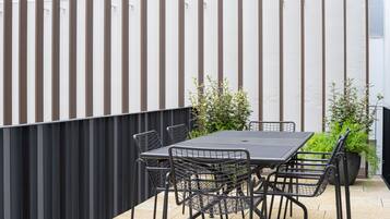 Terrassa exterior amb taula i cadires, tanca de metall negre i vegetació.