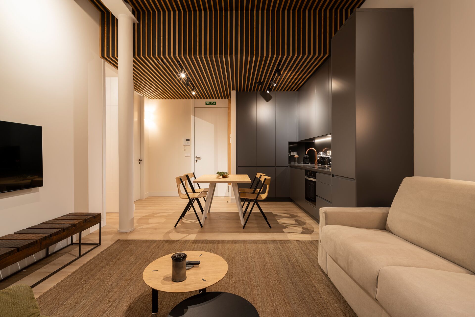 A modern living room with a sofa, a coffee table, a TV, and a dining area with chairs and a table.