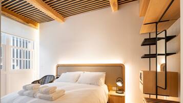 Habitación de hotel con cama, mesita de noche, lámpara y vistas al exterior.