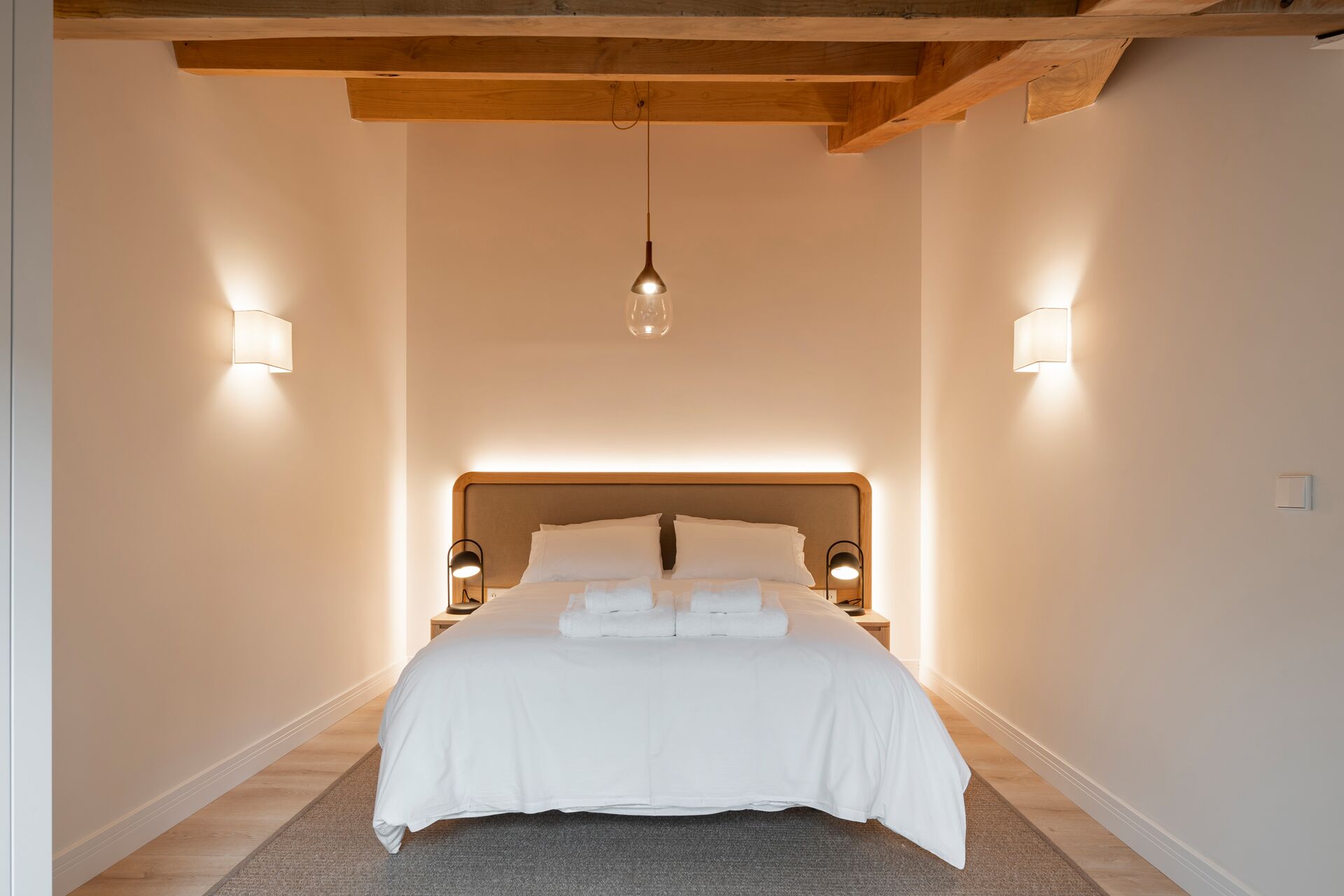 A bedroom with a large bed, two bedside lamps, and a hanging light fixture.
