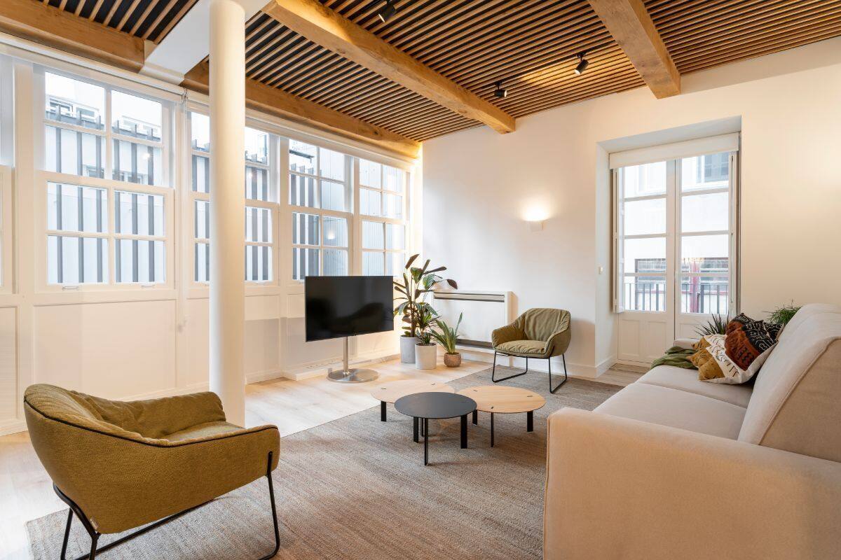 A modern living room with a large TV, comfortable seating, and large windows.