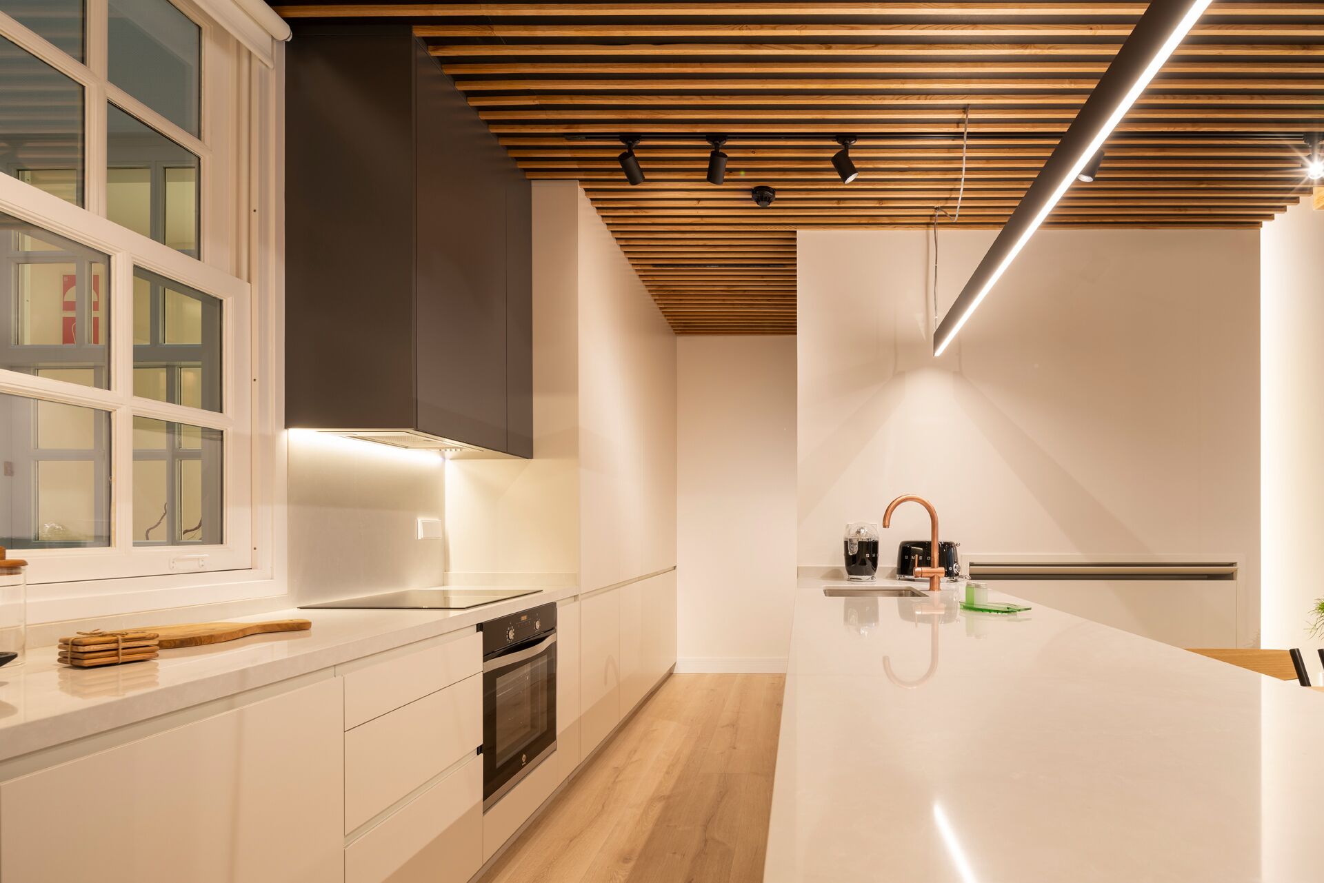 Una cocina moderna con horno integrado, un ventanal grande y techo de madera.