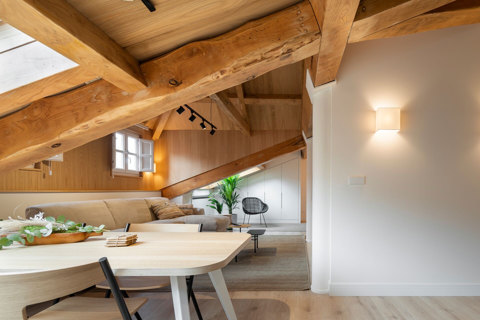 Habitación en el ático con vigas de madera a la vista, una mesa de comedor, sillas, un sofá y una butaca.