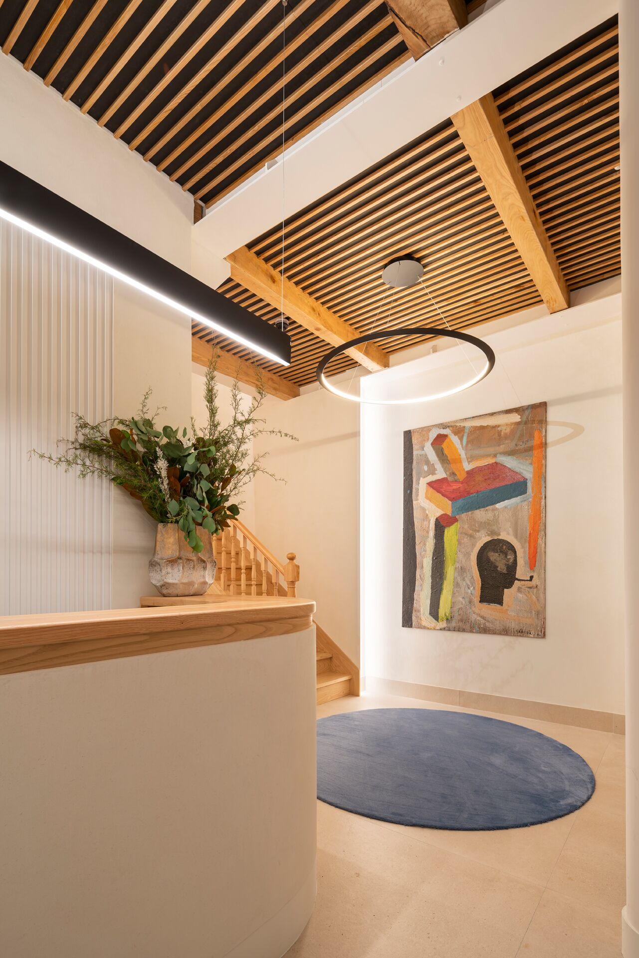 A modern interior with a wooden staircase, a blue rug, and a colorful abstract painting on the wall.