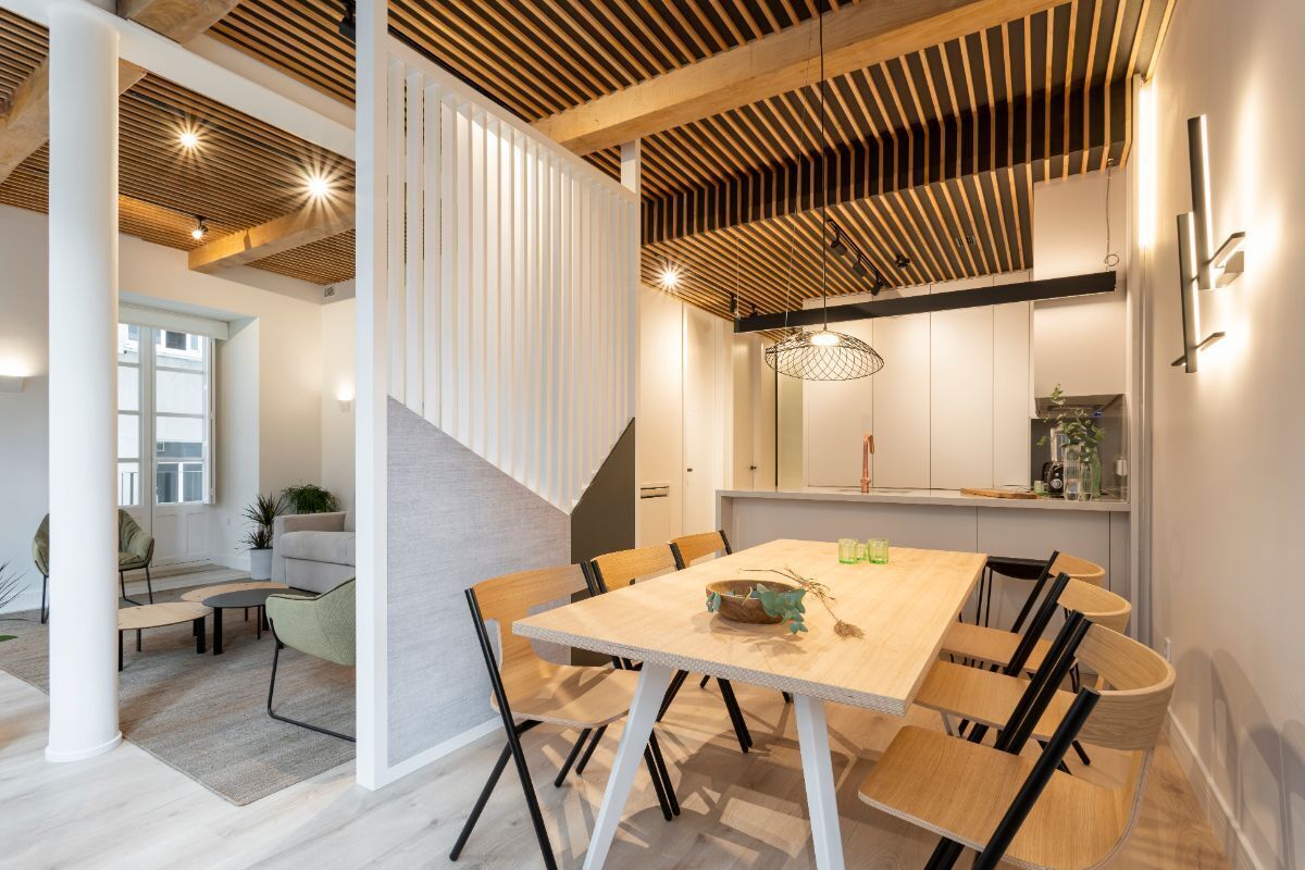 A modern interior with a wooden ceiling, a dining table with chairs, and a staircase.