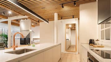A modern kitchen with wooden ceiling beams, a large island with a sink, and a view into a bedroom.