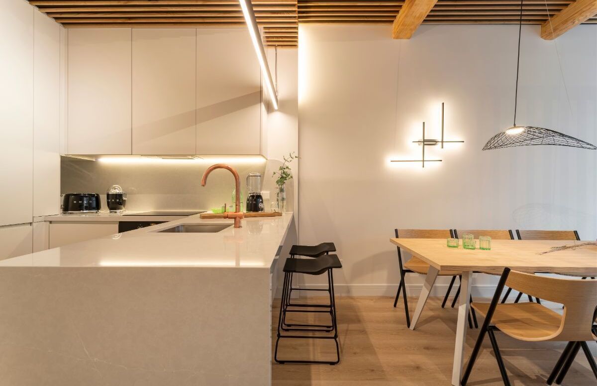 A modern kitchen with a central island, bar stools, and a dining table with chairs.