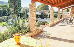 Relax in a serene garden setting with a patio featuring a pergola, round table, and comfortable seating.