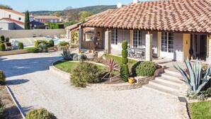 A villa with a tiled roof, a stone facade, and a well-maintained garden with various plants and a gravel driveway. - Beautiful home in Espeluche (Espeluche)