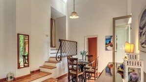 Un área de comedor con una mesa y sillas de madera, una escalera con barandilla y una lámpara colgante.