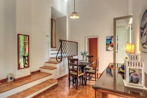 A dining area with a wooden table and chairs, a staircase with a railing, and a hanging light fixture. - Positano: Casa Ligea--in a beautiful old villa, in the heart of Positano (Positano)