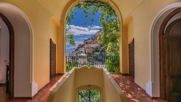 Un pasillo con una vista abovedada que da a un balcón con vistas a un pueblo costero.