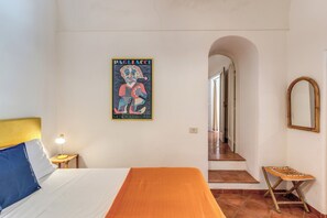 A bedroom with a bed, a nightstand, a lamp, a poster, a mirror, and a staircase. - Positano: Casa Ligea--in a beautiful old villa, in the heart of Positano (Positano)