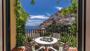 Un balcón con mesa y sillas, con vistas a un pueblo en la ladera y al mar.