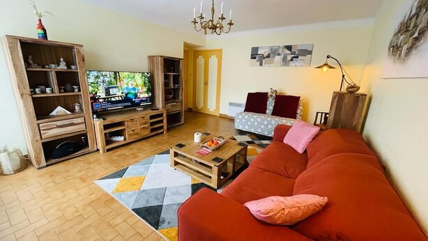 Een woonkamer met een rode bank, een houten tv-meubel en een televisietoestel.