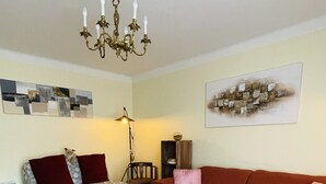 Een woonkamer met een bank, een rode slaapbank, een salontafel, een kroonluchter en een vloerkleed.