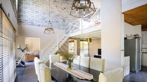 Un vaste espace à manger avec un haut plafond, un escalier et une cuisine visible au fond.