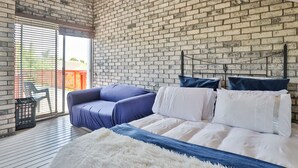 Une chambre avec un mur en briques, un lit avec une literie blanche et bleue, un canapé bleu et un tapis blanc et moelleux.