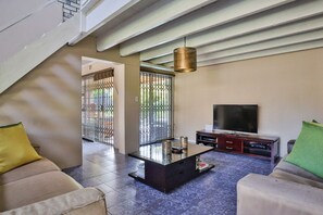 A living room with a sofa, a coffee table, a TV, and a staircase. - Fairview Crescent 03 by CTHA (Cape Town)