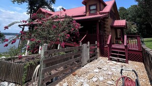 A log cabin with a red roof, a wooden deck, and a view of a lake. - Lake Eufaula Log Cabin, Private Dock, Premier Hunting (Georgetown)