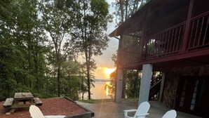 An outdoor seating area with Adirondack chairs and a stone fire pit, overlooking a body of water and trees. - Lake Eufaula Log Cabin, Private Dock, Premier Hunting (Georgetown)