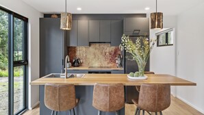 Een moderne keuken met een centraal eiland, barkrukken, hanglampen en uitzicht op het buiten.