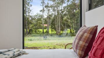 A bedroom with a large window offering a view of a grassy area and trees.