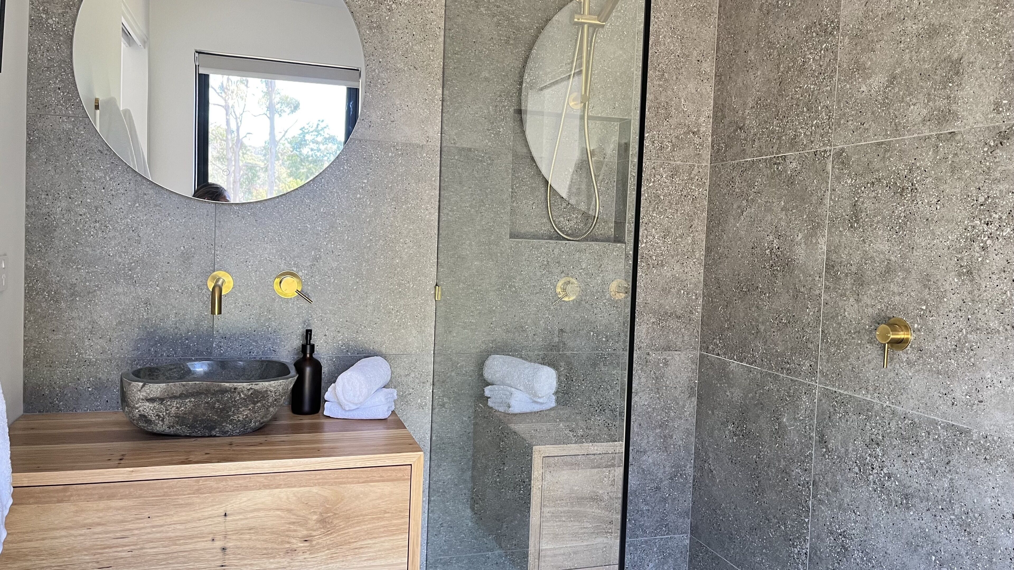 A bathroom with a stone sink, a mirror, and a shower area.