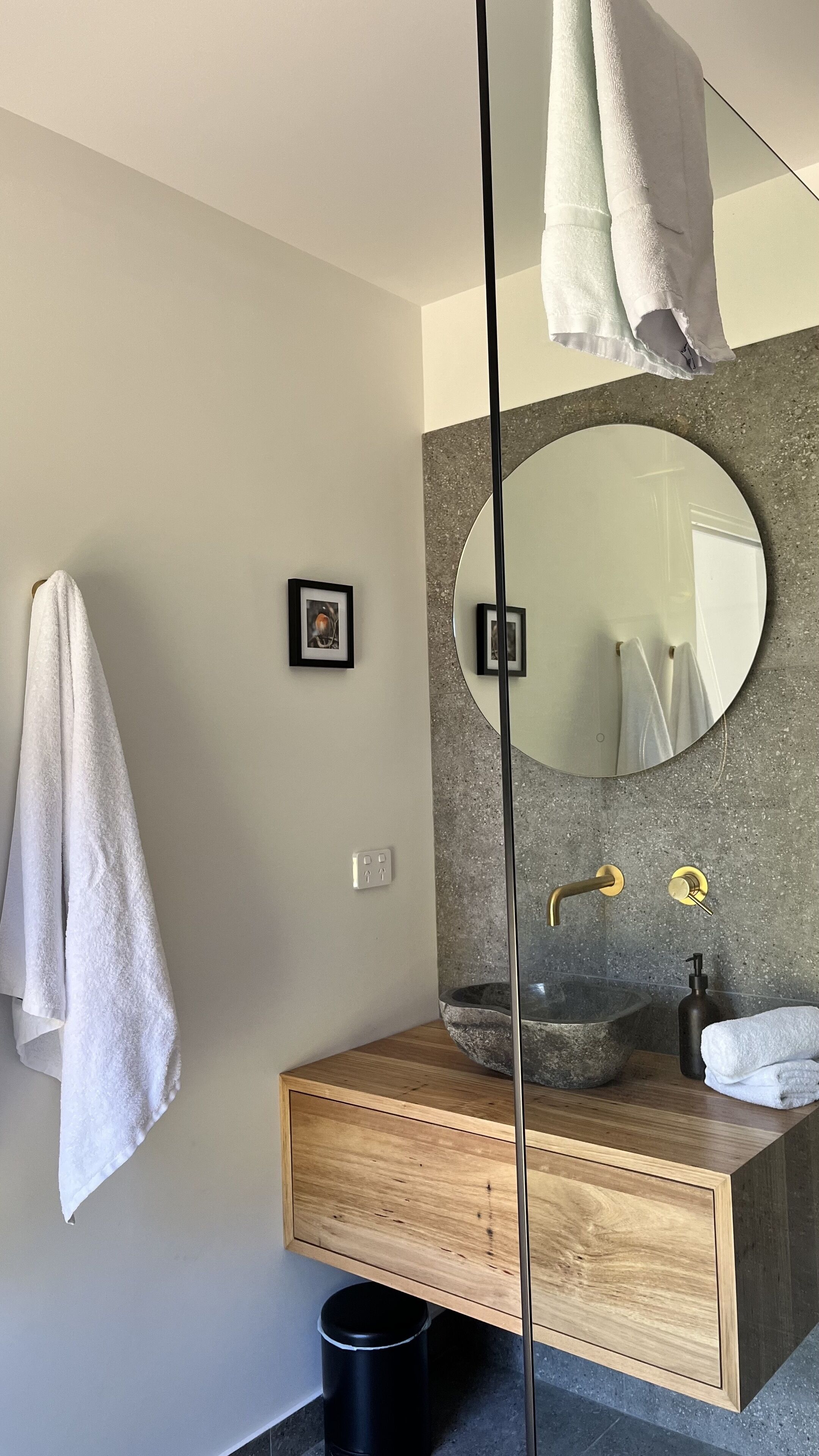 Une salle de bain moderne avec un meuble-lavabo en bois, un miroir rond et un vasque en pierre.