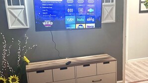 Ein Schlafzimmer mit einem Bett, einem an der Wand befestigten Fernseher, der Streaming-Dienste anzeigt, und einer Kommode mit Schubladen.